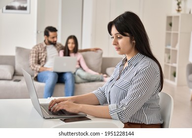 Young Indian Woman Wife And Mother Remote Working Online From Home Office While Family Spending Time At Home. Busy Parent Mom Using Laptop Computer Sitting At Table In Homeoffice.