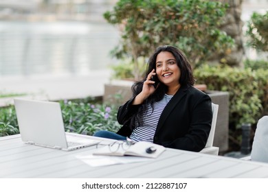 A Young Indian Woman Is Working On A Laptop On The Terrace In A Cafe And Talking On The Phone. Online Business, Freelance.