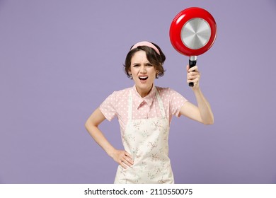 Young indignant angry abuse housewife housekeeper chef cook baker woman in pink apron threatening with red frying pan shout isolated on pastel violet background studio Cooking food process concept.