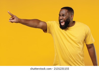 Young indignant angry furious sad stressed happy black man 20s wearing bright casual t-shirt point index finger aside scream isolated on plain yellow color background studio. People lifestyle concept