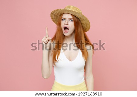 Young indignant caucasian smart intelligent redhead woman 20s ginger long hair wear straw hat summer clothes pointing finger up making remark isolated on pastel pink color background studio portrait.