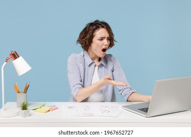Young indignant confused secretary employee business woman in casual shirt sit work at white office desk use pc laptop computer internet online spread hands isolated on pastel blue background studio