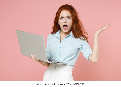 Young indignant confused shocked student businesswoman secretary redhead freelancer woman 20s in blue shirt holding laptop pc computer spread hands isolated on pastel pink background studio portrait