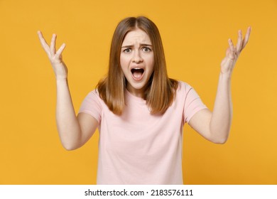 Young indignant shocked expressive angry woman 20s in casual basic pastel pink t-shirt, blank print design look camera spread hand shouting scream isolated on yellow color background studio portrait.