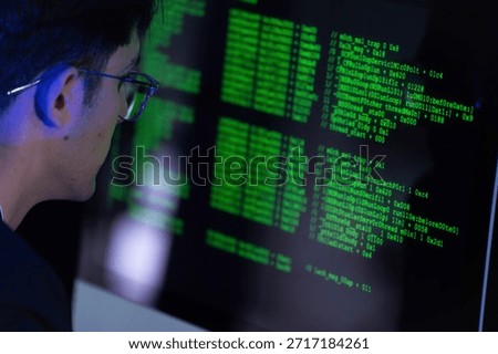 A young individual is focused on coding while sitting in a dimly lit room. The computer screen displays green text, indicating programming activity at night.