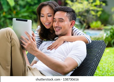 Young Indonesian Couple - Man And Woman - Sitting With A Tablet Computer In The Garden