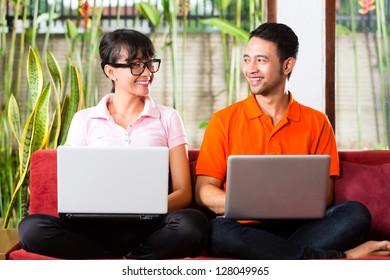 Young Indonesian couple sitting with laptops on a couch, maybe the have an idea or inspiration