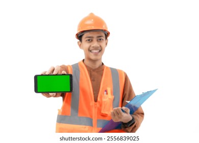 Young Indonesian male construction worker in full safety gear showing green screen of mobile phone to camera, construction and industry advertisement, construction and industry concept, isolated. - Powered by Shutterstock