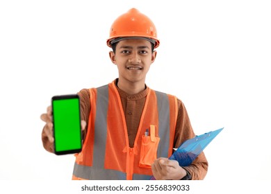 Young Indonesian male construction worker in full safety gear showing green screen of mobile phone to camera, construction and industry advertisement, construction and industry concept, isolated. - Powered by Shutterstock