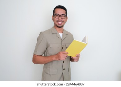 Young Indonesian teacher smiling happy at the camera while holding a book - Shutterstock ID 2244464887