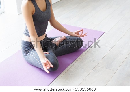 Young indonesian woman meditating, doing yoga lotus pose and asana. Fitness girl enjoying yoga indoors in sport clothes, working out in gym class