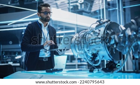 Young Industrial Engineer Working on a Futuristic Jet Engine, Standing with Laptop Computer in Scientific Technology Lab. Scientist Developing a New Electric Motor in a Research Facility.