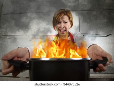 Young Inexperienced Home Cook Woman In Panic With Apron Holding Pot Burning In Flames With Stress And Panic Face Expression In Fire In The Kitchen And Amateur Newbie Rookie Ad Messy Cooking Concept