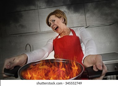 Young Inexperienced Home Cook Woman In Panic With Apron Holding Pot Burning In Flames With Stress And Panic Face Expression In Fire In The Kitchen And Amateur Newbie Rookie Ad Messy Cooking Concept