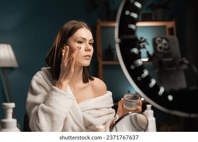 Young influencer woman creating social media videos while applying cream face mask recording video on smartphone. Technology, cosmetics and fashion concept. Copy space - Powered by Shutterstock