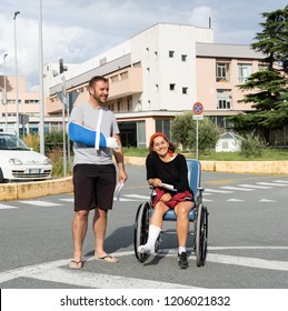 Young injured couple with broken foot and arm coming out of the hospital happy that their insurance paid the medical bills in travel health insurance concept.