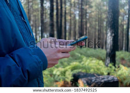 Young inrecognizable man using a mobile phone in the nature wearing a blue coat