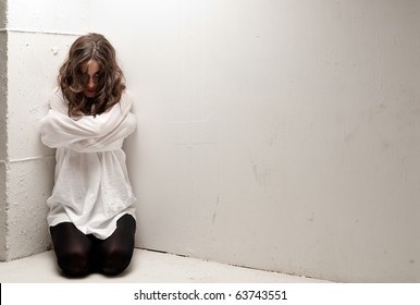 Young insane woman with straitjacket on knees looking at camera