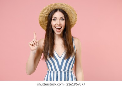 Young insighted smart proactive woman 20s wear summer clothes striped dress straw hat holding index finger up with great new idea isolated on pastel pink background studio. People lifestyle concept