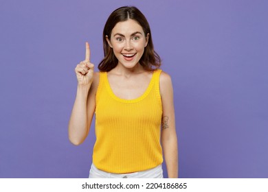 Young Insighted Smart Proactive Woman She Wear Yellow Tank Shirt Holding Index Finger Up With Great New Idea Isolated On Plain Pastel Light Purple Background Studio Portrait. People Lifestyle Concept