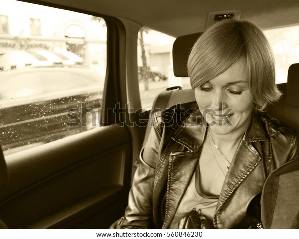 Young intelligent business\
woman sitting inside the car. She is glad, happy and smiling.\
Outside the window of the car - city street. Copy space to add\
text. Sepia.