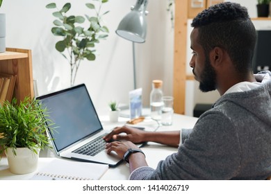 Young Intercultural College Student Looking At Laptop Display While Pressing Keys Of Keypad During Work Over Thesis Or Report