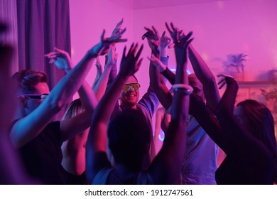 Young Intercultural Glamorous Friends Raising Their Arms While Dancing Together At Home Party In Living-room Illuminated With Pink Lighting