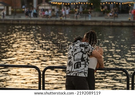 Young interethnic couple hugging and kissing on the city embankment at sunset on a summer day in Gdansk, love, friendship, romance, street photography