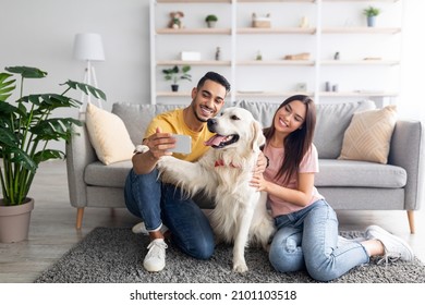 Young International Couple Taking Mobile Selfie With Pet Dog On Smartphone At Home, Copy Space. Full Length Of Millennial Spouses Making Photo With Golden Retriever, Having Fun Together Indoors