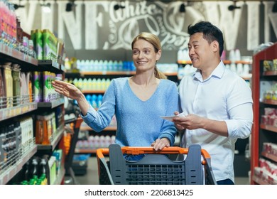 A Young International Couple, A Woman And An Asian Man Walk With A Shopping Cart In A Supermarket