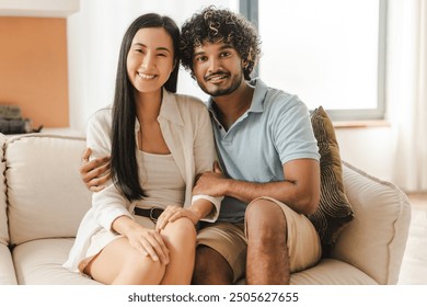 Young interracial couple, Asian woman and Indian man relaxing and embracing on sofa at home looking at camera. Relationship concept - Powered by Shutterstock