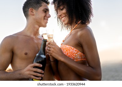 Young interracial couple with caucasian man and African descent woman celebrating date on the beach drinking champagne and watching each other tenderly. - Powered by Shutterstock