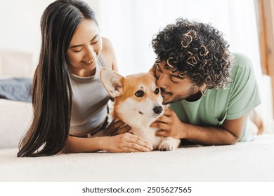 Young interracial couple cuddles with their corgi dog on a cozy carpet, radiating love and happiness at home - Powered by Shutterstock