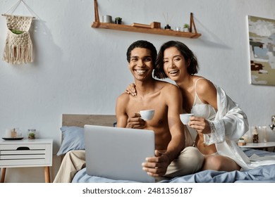 A young interracial couple enjoys their morning coffee while using a laptop in their bedroom. - Powered by Shutterstock