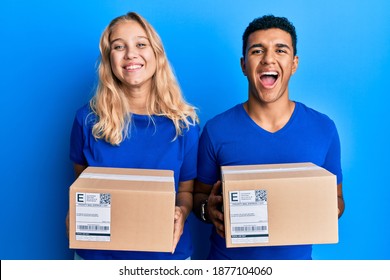 Young Interracial Couple Holding Delivery Package Smiling And Laughing Hard Out Loud Because Funny Crazy Joke. 