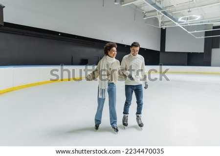 Young interracial couple holding hands while ice skating on rink 