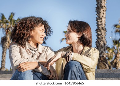 Young Interracial Couple Of Homosexual Women Talking Sitting On The Stairs, Concept Of Sexual Freedom And Racial Diversity