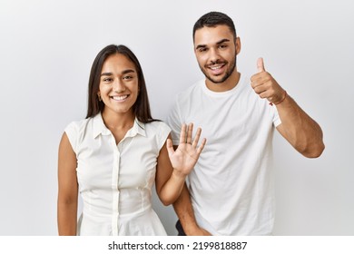 Young interracial couple standing together in love over isolated background showing and pointing up with fingers number six while smiling confident and happy. 