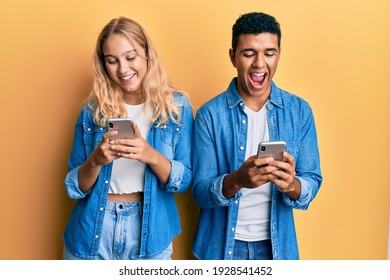 Young Interracial Couple Using Smartphone Smiling And Laughing Hard Out Loud Because Funny Crazy Joke. 