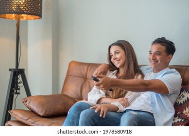 Young Interracial Couple Watching Tv Together Sitting On The Sofa At Home - Couple Life And Happy Lifestyle People Having With Movie - Indoor Leisure Activity Black Boy And Caucasian Girl In Love 