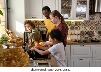 Young Interracial Family Of Father, Mother And Two Sons Washing Fresh Vegetables In The Kitchen