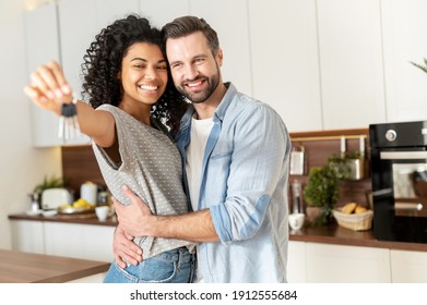 Young interracial married couple homeowners smiling, showing keys from a new apartment, hugging and looking at the camera, standing in the kitchen and celebrating moving in a new home, family concept - Shutterstock ID 1912555684
