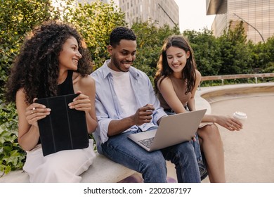 Young interracial men and women use tablet, computer laptop in street near college. Brunette students wear casual clothes spring. Concept of modern learning - Shutterstock ID 2202087197