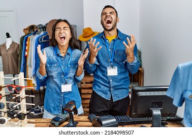 Young interracial people working at retail boutique crazy and mad shouting and yelling with aggressive expression and arms raised. frustration concept. 