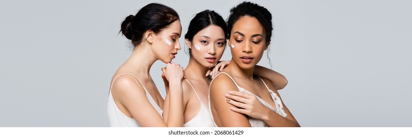 Young interracial women with cream on faces posing isolated on grey, banner - Powered by Shutterstock