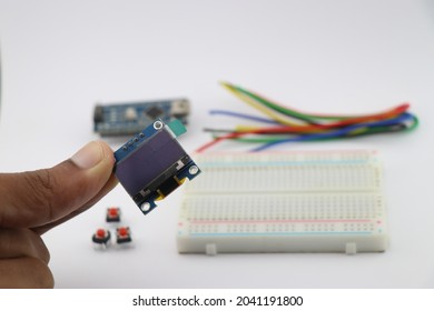 Young inventor holding OLED display in hand, Arduino display module with breadboard and wires on background showing creative electronic projects concept