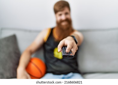 Young Irish Man Smiling Happy Watching Basketball Game On Tv At Home.