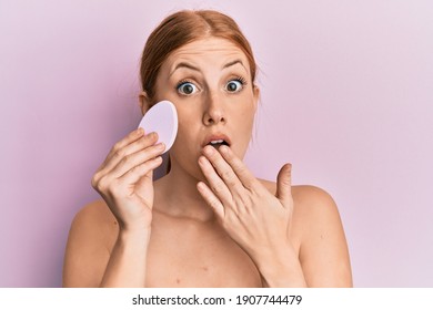 Young Irish Woman Holding Makeup Sponge Covering Mouth With Hand, Shocked And Afraid For Mistake. Surprised Expression 