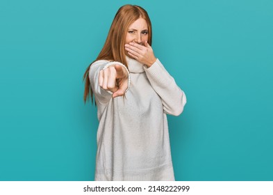 Young Irish Woman Wearing Casual Winter Sweater Laughing At You, Pointing Finger To The Camera With Hand Over Mouth, Shame Expression 