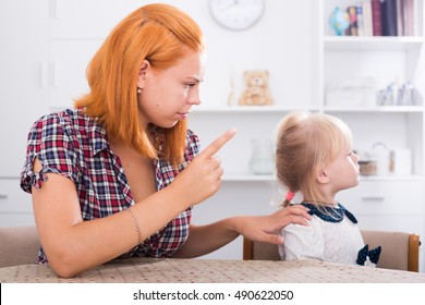 Young irritated woman sitting and scolding daughter indoors